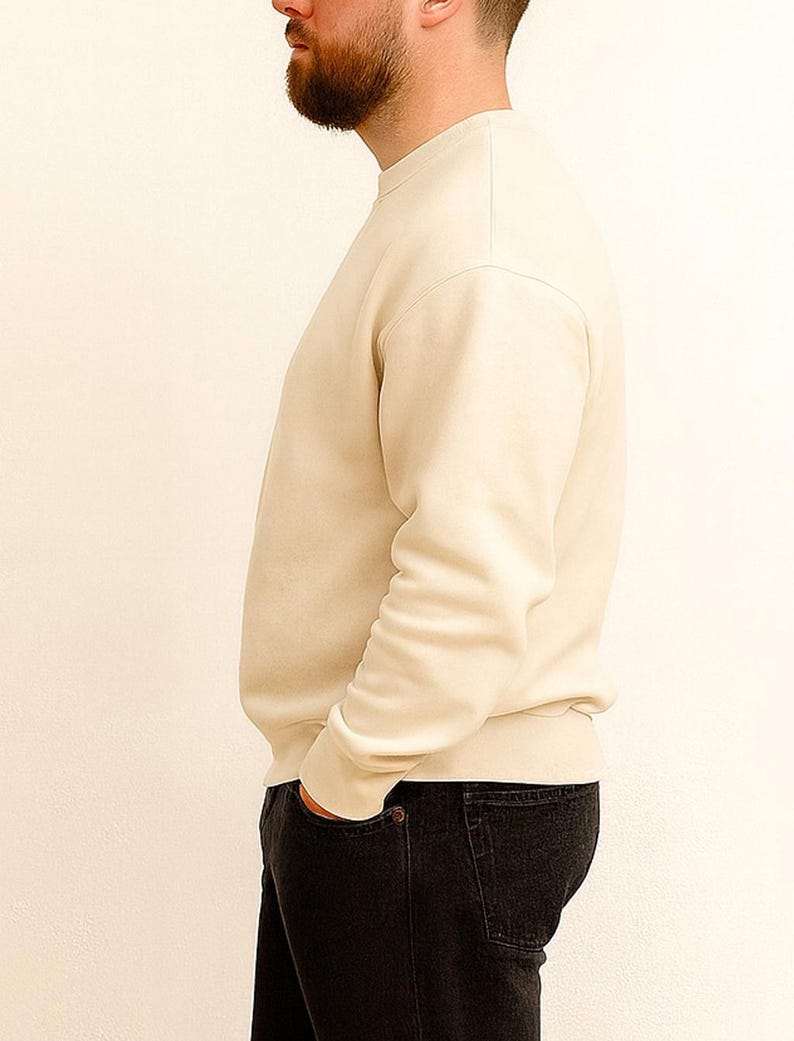 Side view of man wearing a beige sweater and black pants against a white background.