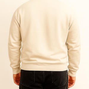 Back view of person wearing a beige sweatshirt and black pants on a plain background.