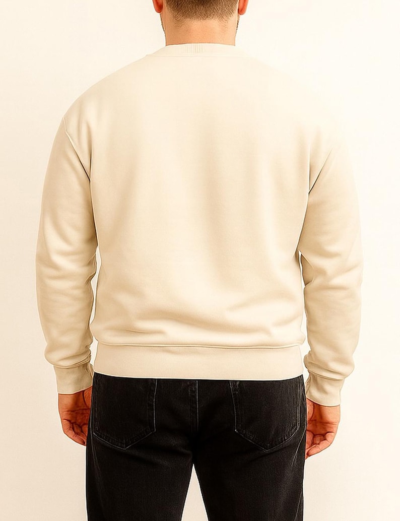 Back view of person wearing a beige sweatshirt and black pants on a plain background.