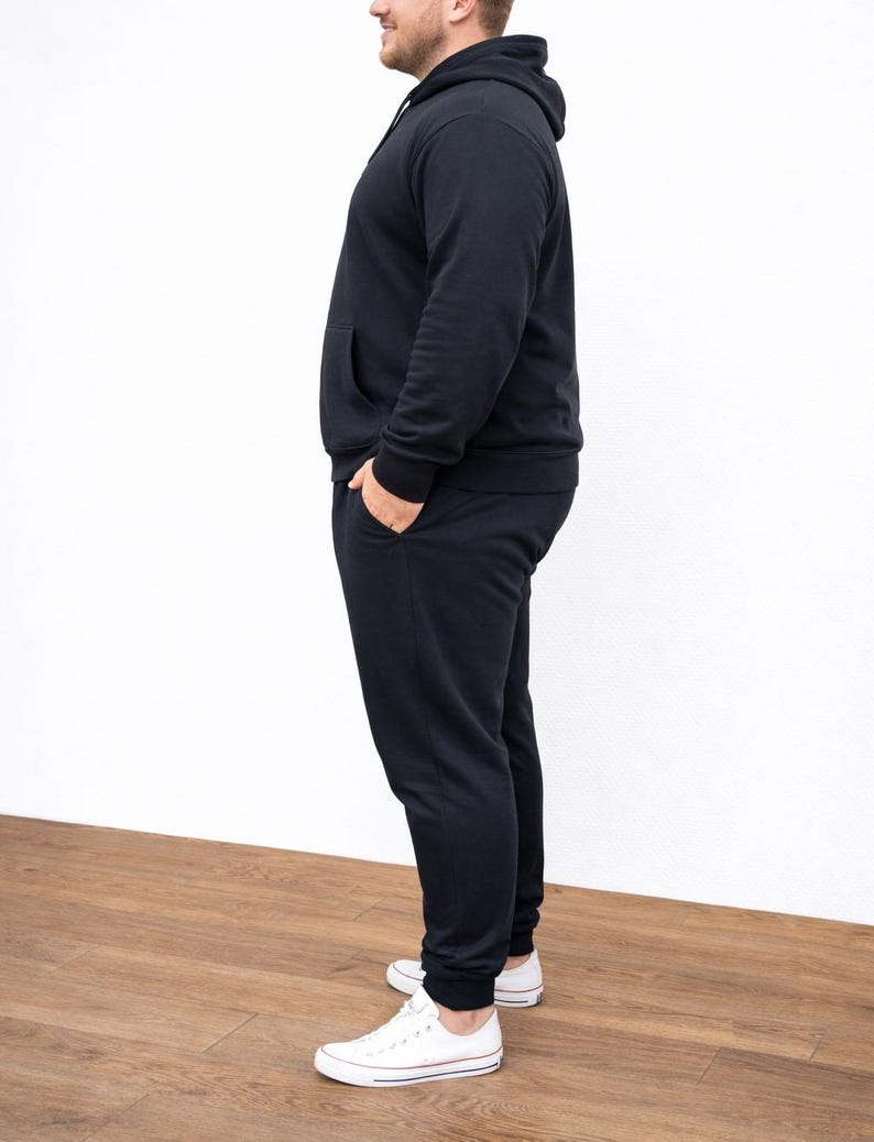 Side view of person wearing a black Plus Size Mens Classic Hoodie and pants with white sneakers on a wooden floor.