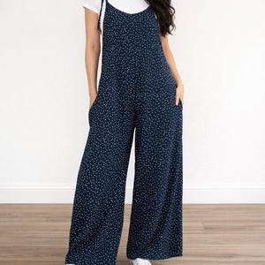 Woman wearing navy Tie Shoulder Jumpsuit with white polka dots and white tee underneath on plain white background.