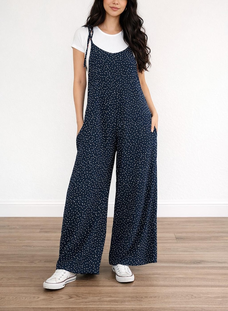 Woman wearing navy Tie Shoulder Jumpsuit with white polka dots and white tee underneath on plain white background.