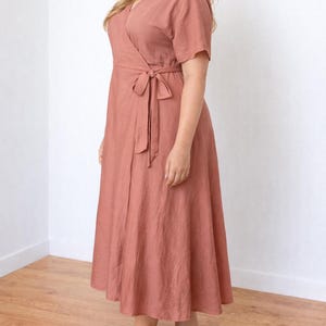 Side view of woman wearing a pink Plus Size Wrap Dress with a white background.