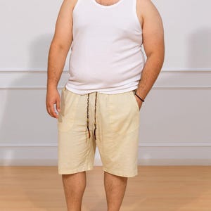 Person wearing white tank top and beige Plus Size Drawstring Knee Length Shorts with plain background and wood flooring.