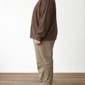 Side view of person wearing a brown Plus Size Button Front Cardigan and beige pants standing against a white wall.