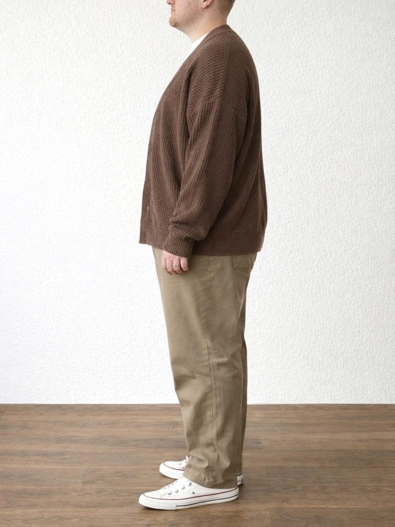 Side view of person wearing a brown Plus Size Button Front Cardigan and beige pants standing against a white wall.