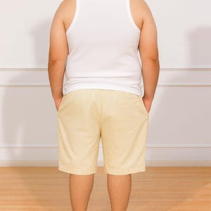Back view of person wearing a white tank top and beige Plus Size Drawstring Knee Length Shorts standing against a plain white wall.