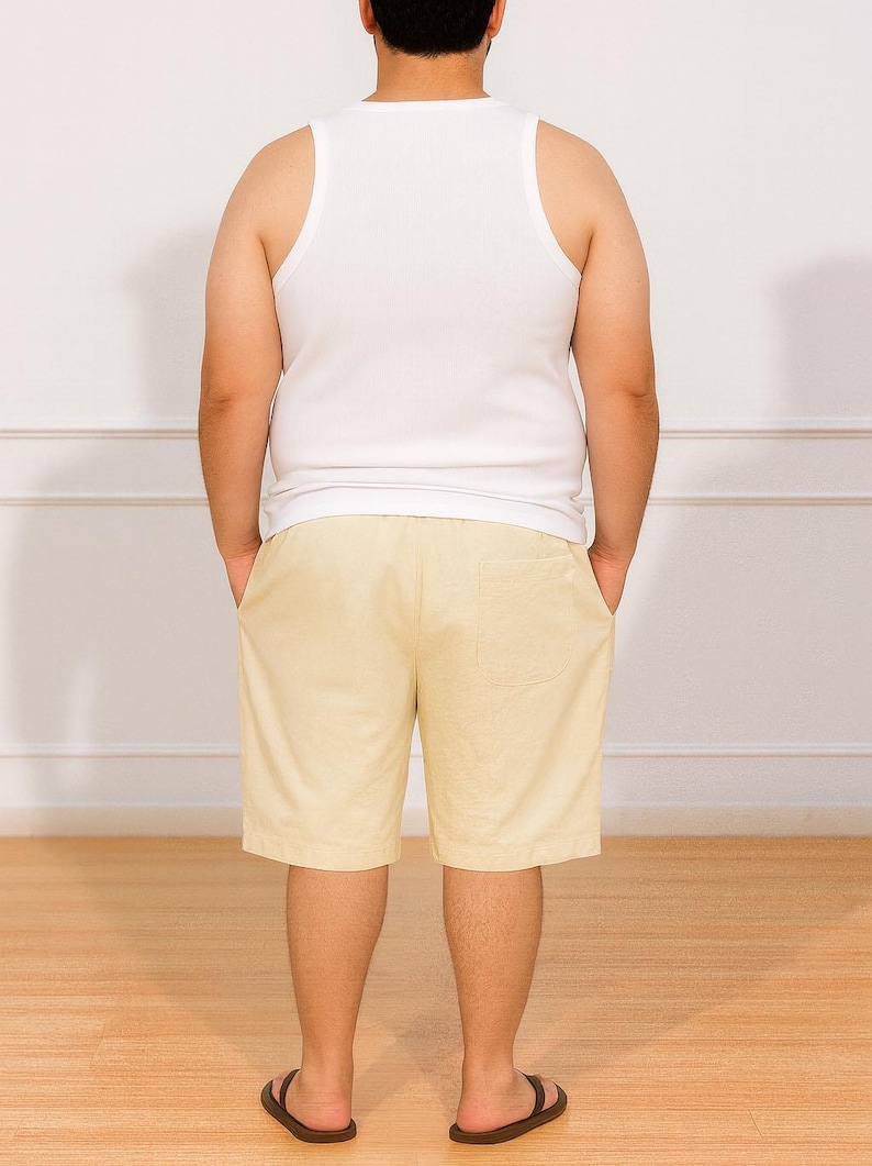 Back view of person wearing a white tank top and beige Plus Size Drawstring Knee Length Shorts standing against a plain white wall.