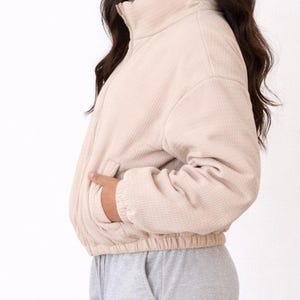Side view of woman wearing a beige Puffer Jacket and gray sweatpants on a white background.