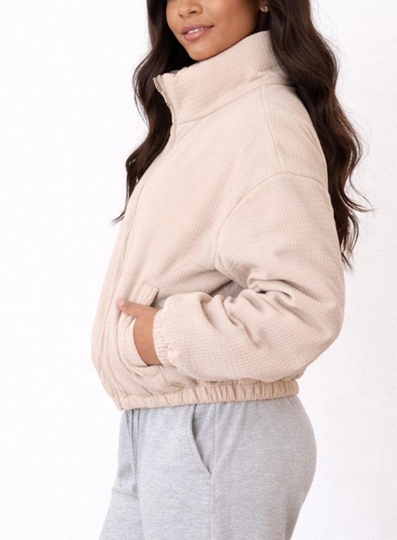 Side view of woman wearing a beige Puffer Jacket and gray sweatpants on a white background.