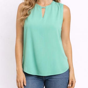 Woman wearing a mint green Keyhole Neckline Sleeveless Top and blue jeans on a white background.