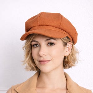 Woman wearing a brown Baker Boy Cap and coat against a white background.