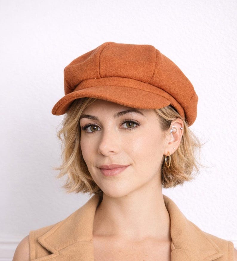 Woman wearing a brown Baker Boy Cap and coat against a white background.