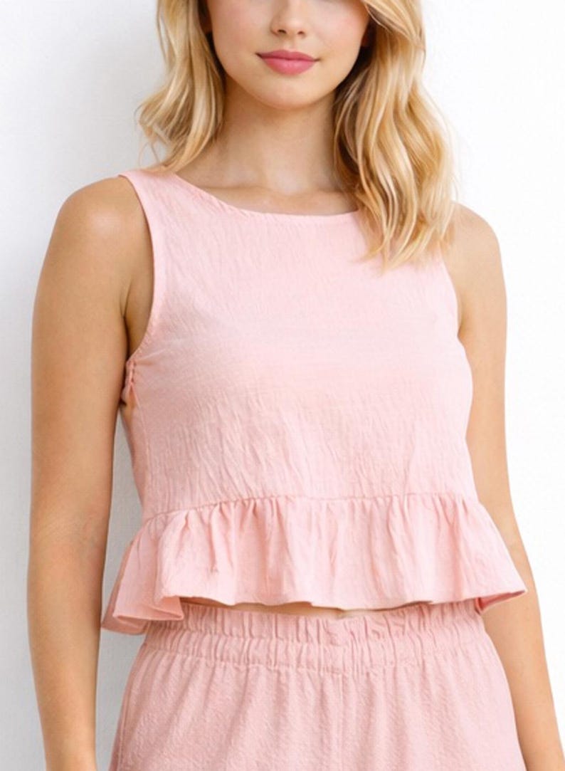 Woman wearing a pink Ruffle Hem Sleeveless Crop Top and pants set on a white background.