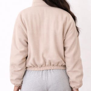 Back view of woman wearing a beige Puffer Jacket and gray sweatpants on a white background.