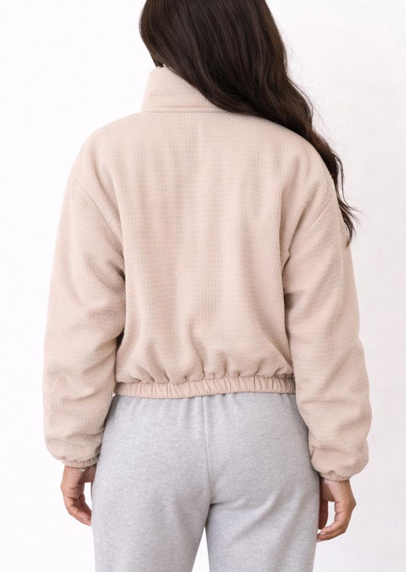 Back view of woman wearing a beige Puffer Jacket and gray sweatpants on a white background.