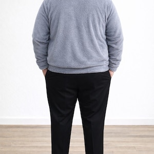 Back view of man wearing a gray Plus Size Mens Bomber Jacket and black pants standing against a white wall.