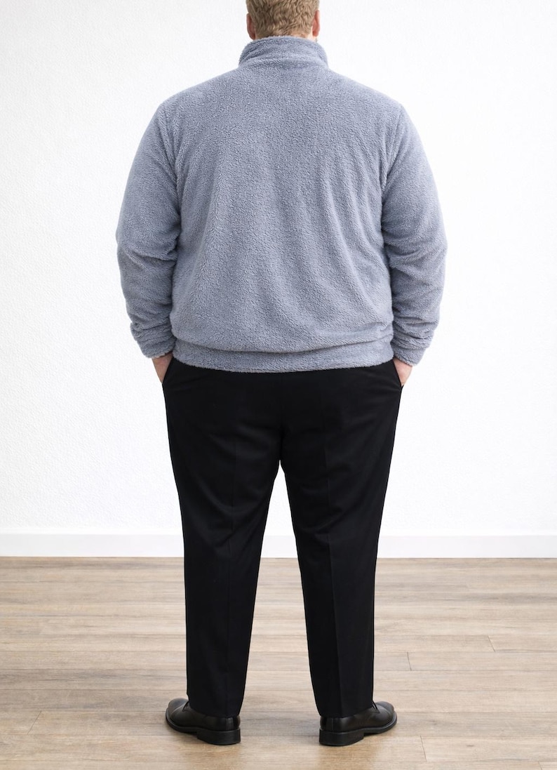 Back view of man wearing a gray Plus Size Mens Bomber Jacket and black pants standing against a white wall.