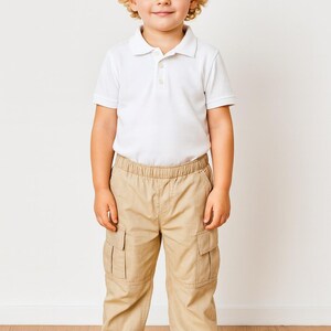 Child wearing a white polo shirt and beige Cargo Pants standing on a wooden floor with a white wall background.
