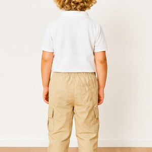 Back view of child wearing a white polo shirt and beige Cargo Pants standing on a wooden floor with a white wall background.