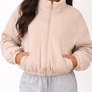 Woman wearing a beige Puffer Jacket and gray sweatpants on a white background.