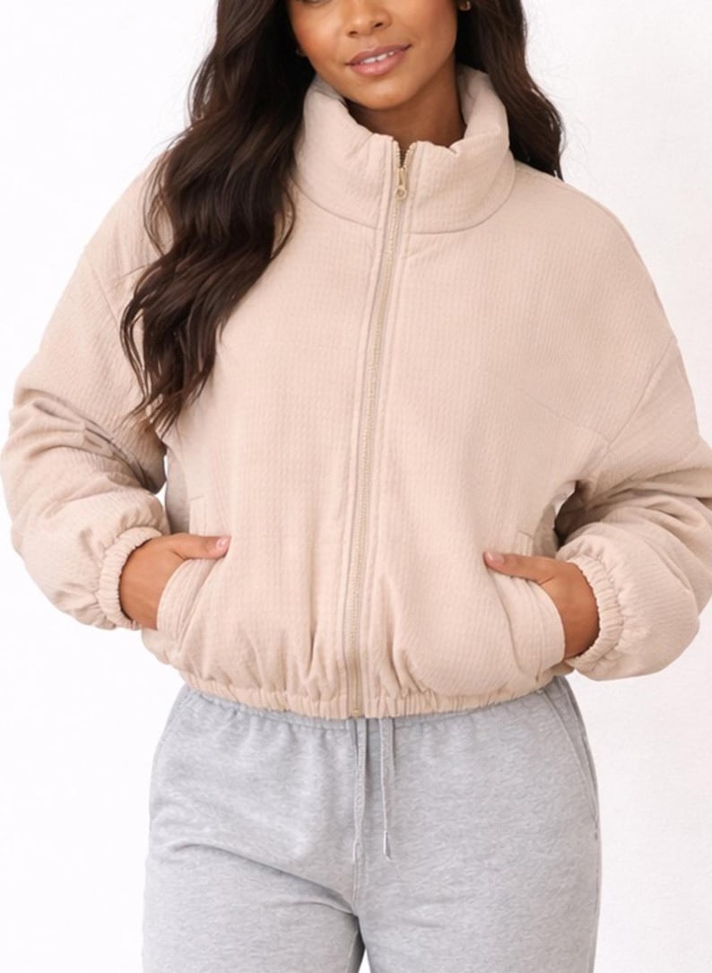 Woman wearing a beige Puffer Jacket and gray sweatpants on a white background.