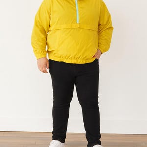 Person wearing a yellow Plus Size Mens Windbreaker Jacket with zipper, black pants, and white shoes on a white background.
