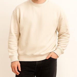 Man wearing a beige sweatshirt and black pants against a white background.