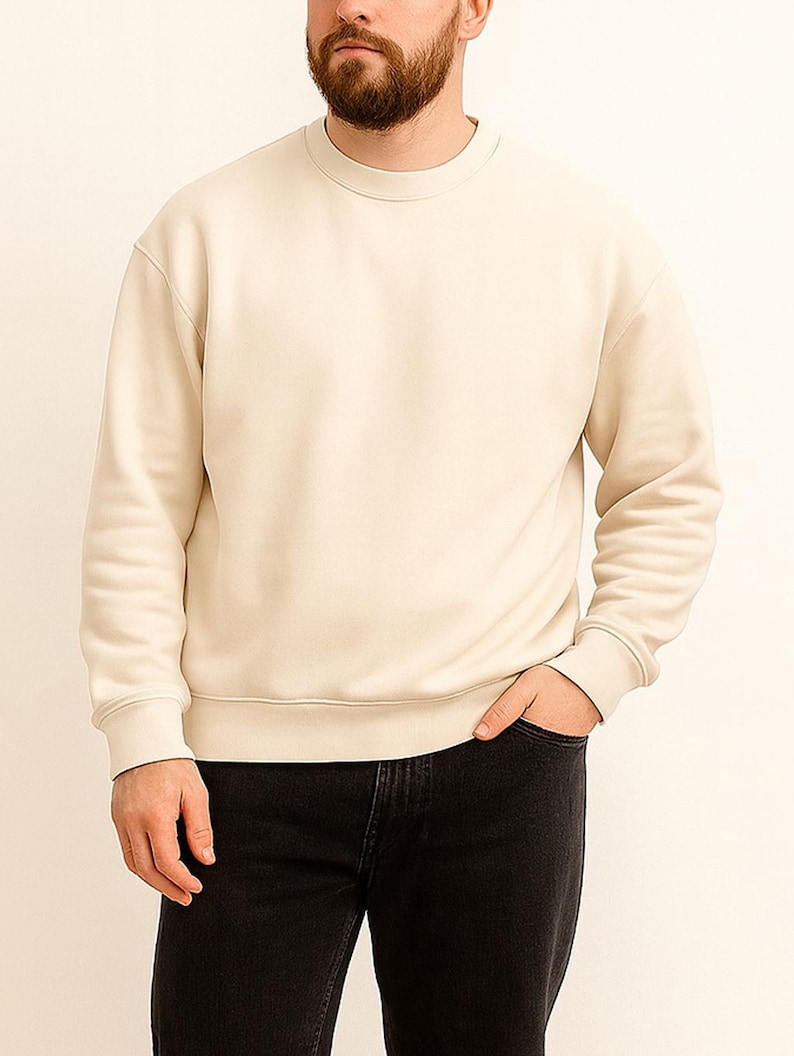 Man wearing a beige sweatshirt and black pants against a white background.