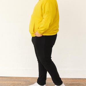 Side view of person wearing a yellow Plus Size Mens Windbreaker Jacket and black pants standing against a white wall.