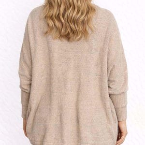 Back view of woman wearing a beige Batwing Sleeve Cardigan and blue jeans on a wooden floor.