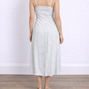 Back view of woman wearing a white floral Milkmaid Midi Cami Dress on a plain background.