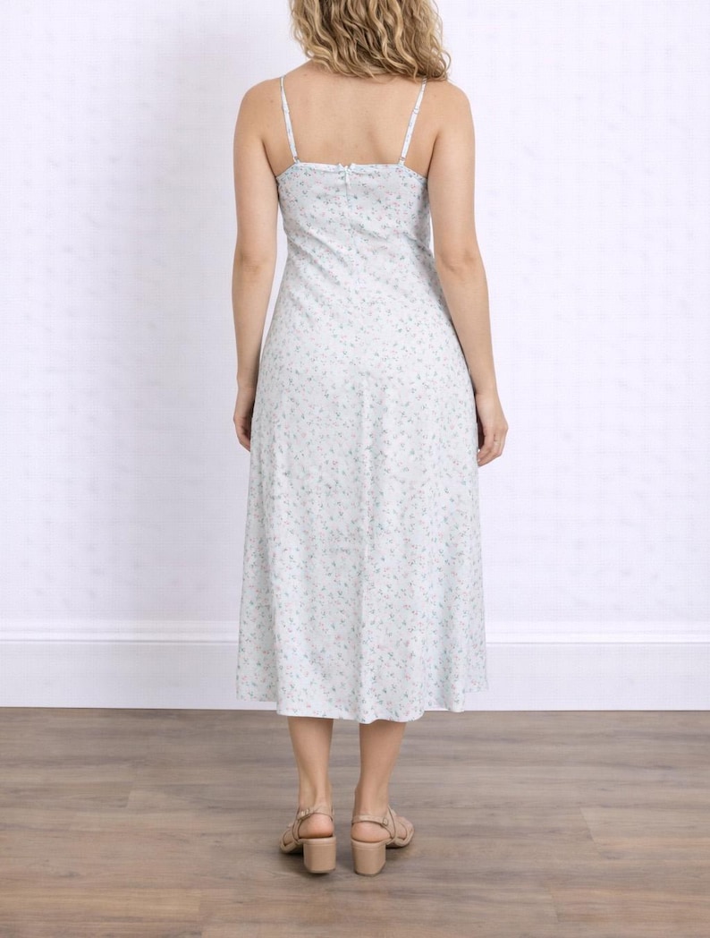 Back view of woman wearing a white floral Milkmaid Midi Cami Dress on a plain background.