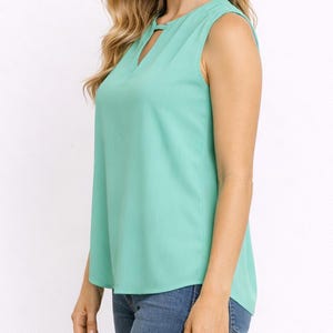Side view of woman wearing a mint green Keyhole Neckline Sleeveless Top and blue jeans on a white background.