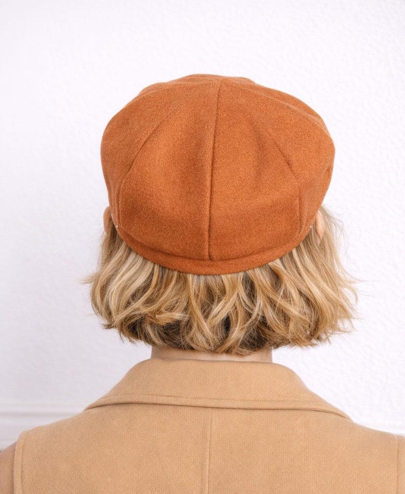 Back view of woman wearing a brown Baker Boy Cap and coat against a white background.