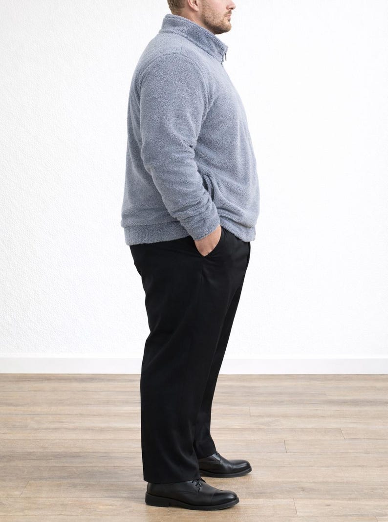 Side view of man wearing a gray Plus Size Mens Bomber Jacket and black pants standing against a white wall.
