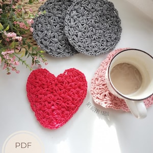 May include: Handmade crochet coasters in different shapes and colors. Two grey, round coasters with a textured pattern are shown with a red heart-shaped coaster and a pink heart-shaped coaster with a mug. The text "PDF Pattern" and "+ Video tutorials" are also visible.