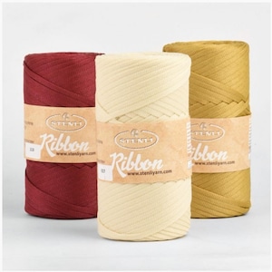May include: Three spools of ribbon in burgundy, cream, and gold. Each spool has a paper label with the word "Ribbon" and the website address www.stenliyarn.com. The ribbon is tightly wound and appears to be made of a woven material.