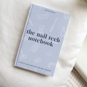 Op de afbeelding: Een lavendelkleurig notitieboekje met de titel "the nail tech notebook" en de tekst "A step by step guide into the nail industry". De omslag heeft illustraties van nagelgereedschap en -benodigdheden.