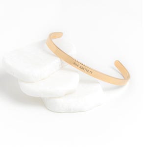 May include: Gold-toned bangle bracelet with the inscription "Rise Above It".