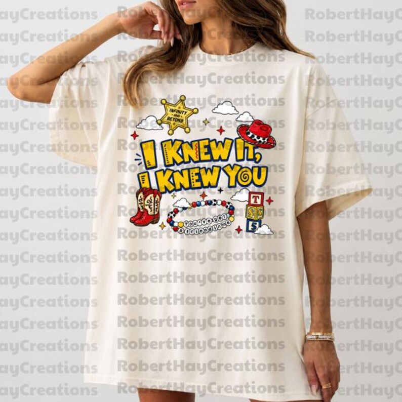 Puede incluir: Una camiseta de manga corta color hueso con un estampado gr&aacute;fico que incluye el texto I KNEW IT, I KNEW YOU. El dise&ntilde;o presenta una estrella de sheriff amarilla, un sombrero de vaquero rojo, botas rojas, una pulsera de cuentas y tres cubos.
