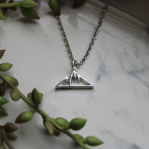May include: A silver necklace with a mountain range pendant. The pendant is a simple outline of a mountain range with a triangular shape.