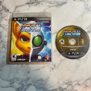 May include: A PlayStation 3 video game case and disc for "Ratchet & Clank Future: A Crack in Time." The case features a split image of the characters Ratchet and Clank. The disc is gold with the game title and logo.