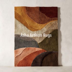 May include: A rectangular rug with a layered design in shades of brown, orange, and green. The rug features a textured surface and a landscape-inspired pattern. The text "Asha Artisan Rugs" is displayed on the rug.