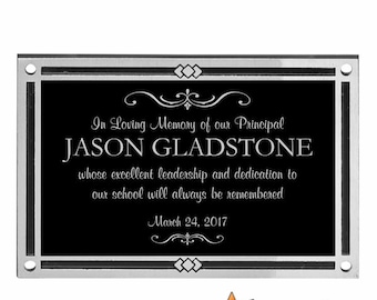 May include: A black plaque with silver trim and a white inscription that reads "In Loving Memory of our Principal JASON GLADSTONE whose excellent leadership and dedication to our school will always be remembered March 24, 2017".