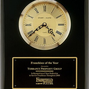 May include: A black plaque with a gold trim and a gold clock face. The plaque reads "Franchisee of the Year Presented to Torrance Property Group In Recognition of Your Dedication to Service Excellence Throughout 2000 Fairfield Inn & Suites by Marriott."