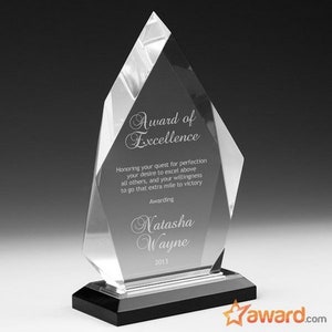 May include: A clear glass award in the shape of a diamond with a black base. The award reads "Award of Excellence" and "Honoring your quest for perfection your desire to excel above all others, and your willingness to go that extra mile to victory." The award is presented to "Natasha Wayne" in 2013.
