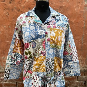 May include: A patchwork pajama set displayed on a black mannequin. The set includes a collared, long-sleeved shirt and drawstring trousers. The fabric is patterned with florals in white, blue, yellow, and red. The background is a textured, reddish-brown wall.