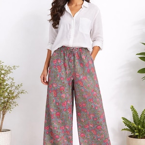 Op de afbeelding: Een persoon draagt een wit overhemd en een broek met bloemenprint. De broek is grijs met een roze bloemenpatroon. De outfit is casual en geschikt voor dagelijks gebruik. De broek heeft wijde pijpen.