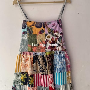 Peut inclure: Une robe d'été patchwork avec une variété de motifs floraux et géométriques dans des tons orange, violet, bleu et vert. La robe a de fines bretelles et une jupe à volants, suspendue à un cintre en bois.